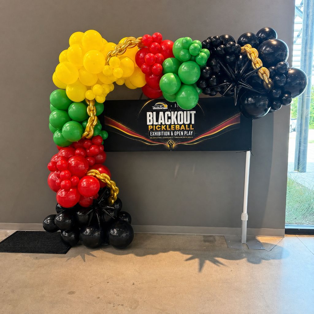 Blackout Pickleball Exhibition balloon arch installation with red, yellow, green, and black balloons